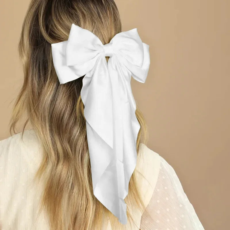 A woman with long blonde hair is shown from the back wearing a white silk bow hair clip.