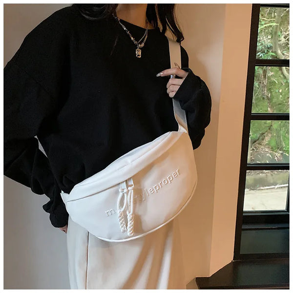 A woman wearing a white leather crossbody saddle bag with a chain strap and a black sweater.