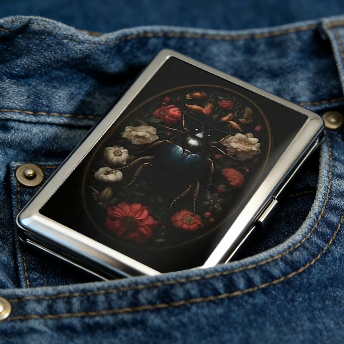 A silver metal card case with an intricate floral design is shown inside a blue denim jean pocket.