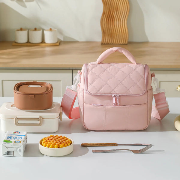 A pink reusable insulated nylon lunch bag is displayed on a table with food and utensils.