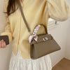 A woman wears a yellow knit sweater and white skirt while holding an elegant taupe leather crossbody clutch bag.