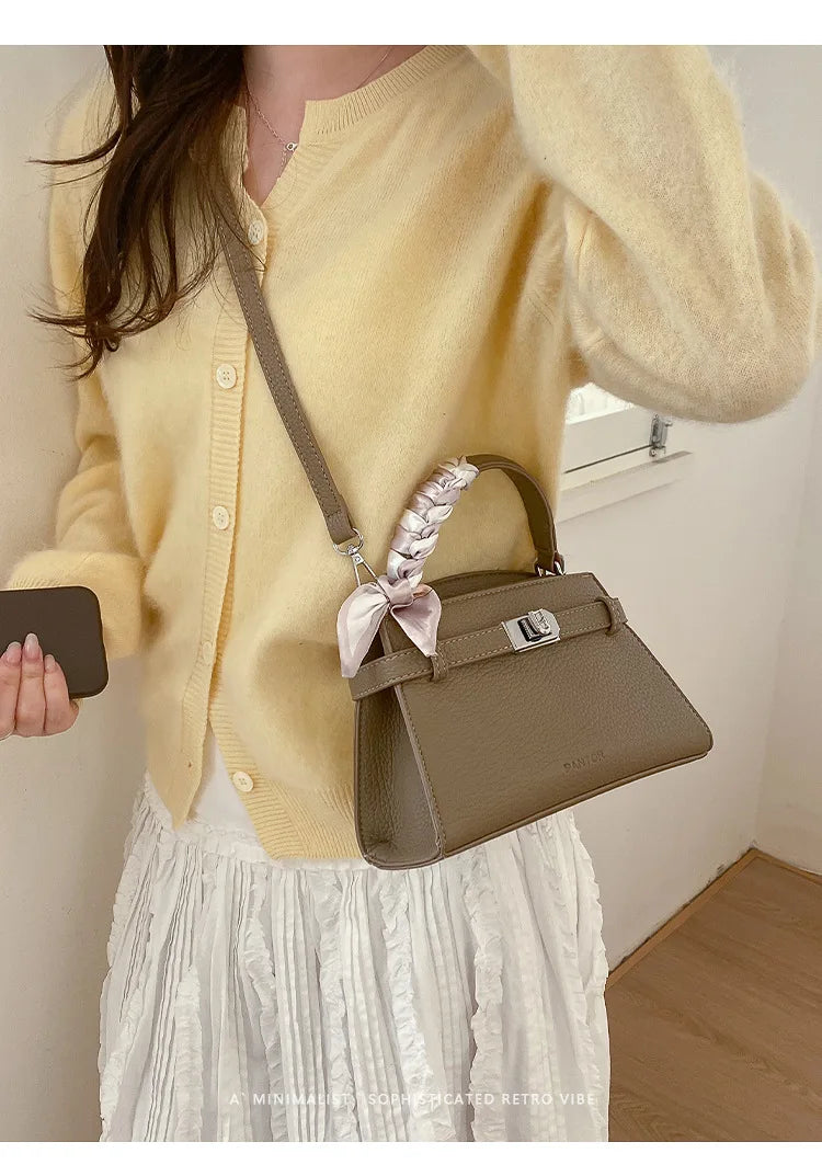 A woman wears a yellow knit sweater and white skirt while holding an elegant taupe leather crossbody clutch bag.
