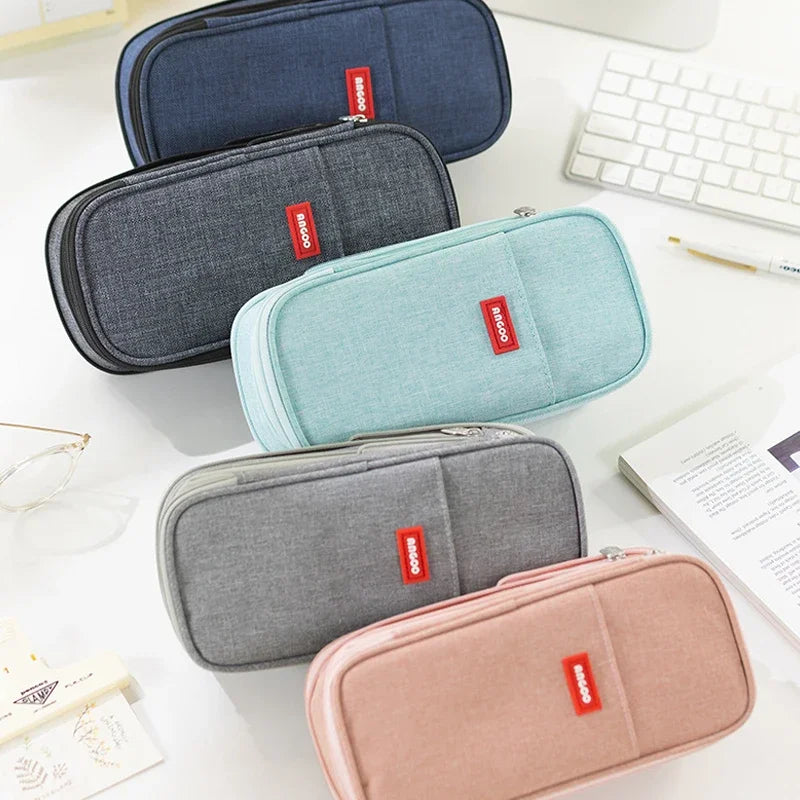 Une collection de cinq trousses en toile pastel et gris empilées sur une surface blanche.