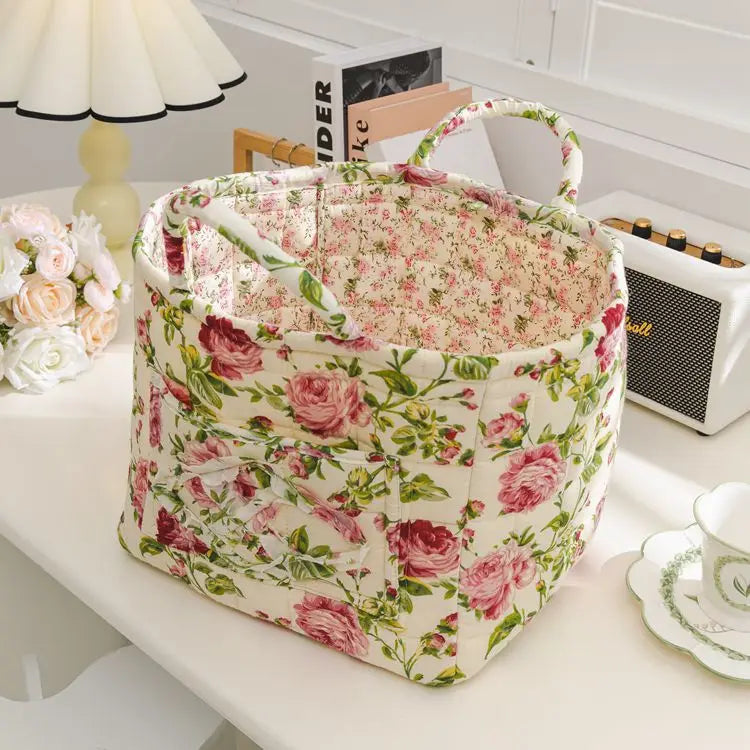 Blumiges Stoff-Aufbewahrungskorb mit Henkeln, rosa und grüne Rosen, auf weißem Tisch.