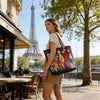 Una joven con top y shorts beige sostiene un bolso de tela acolchado vintage colorido frente a la Torre Eiffel.