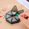 A black weekly pill organizer divided into seven days, with pills visible in the compartments and a hand holding it.