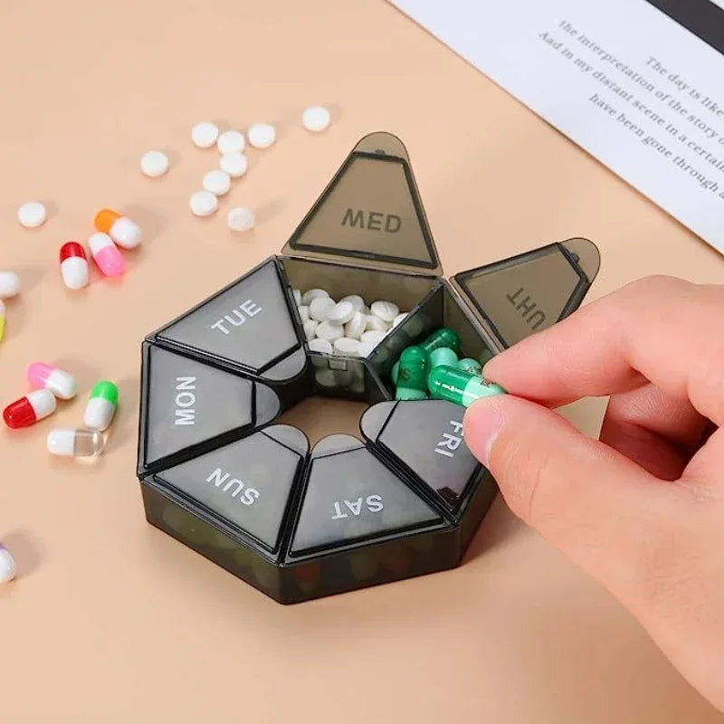 A black weekly pill organizer divided into seven days, with pills visible in the compartments and a hand holding it.
