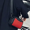 A black jacket sleeve holds a red and black punk riveted crossbody sling bag.