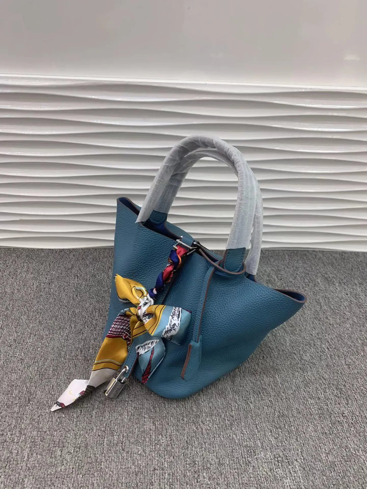 Türkis-Leder-Korbtasche mit grauem Schnur und farbenfrohen Stoffakzenten auf grauem Teppich.
