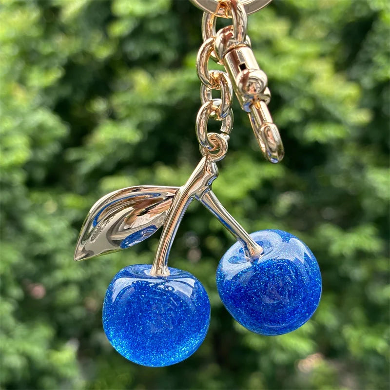 Gold chain keychain featuring a blue glitter crystal apple charm hanging against a green background.