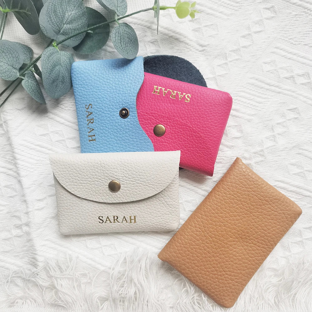 A collection of five genuine leather card holders and coin purses in various shades of blue, pink, beige, and brown resting o