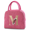 A pink insulated canvas lunch bag with a gold letter M print.