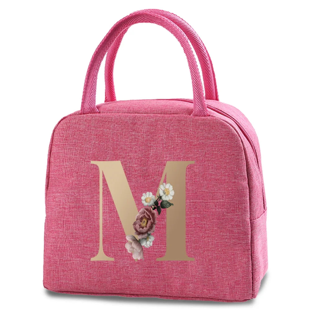 A pink insulated canvas lunch bag with a gold letter M print.