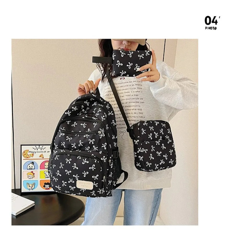 A woman holds a black nylon travel backpack featuring a white bow print on it.