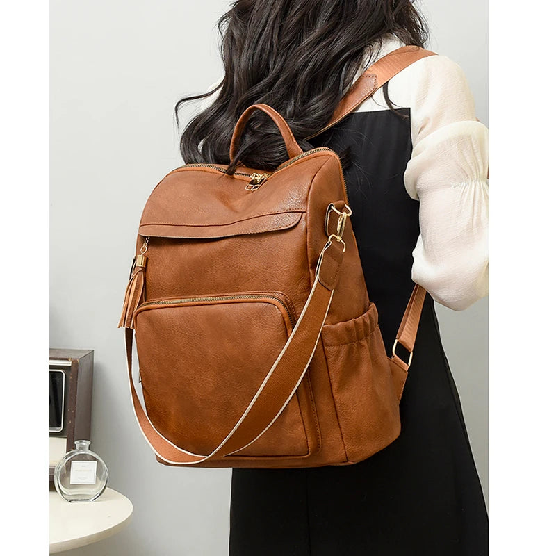 A brown vintage tassel backpack is shown carried by a person wearing a black dress and a cream-colored sleeve.