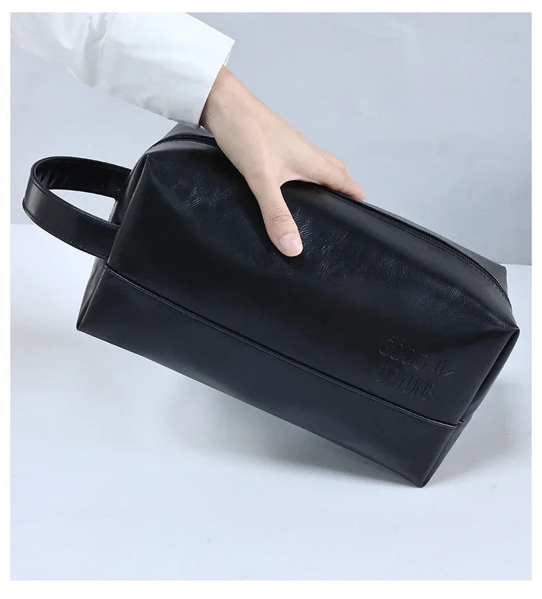 A hand is holding a black portable PU leather cosmetic organizer bag.
