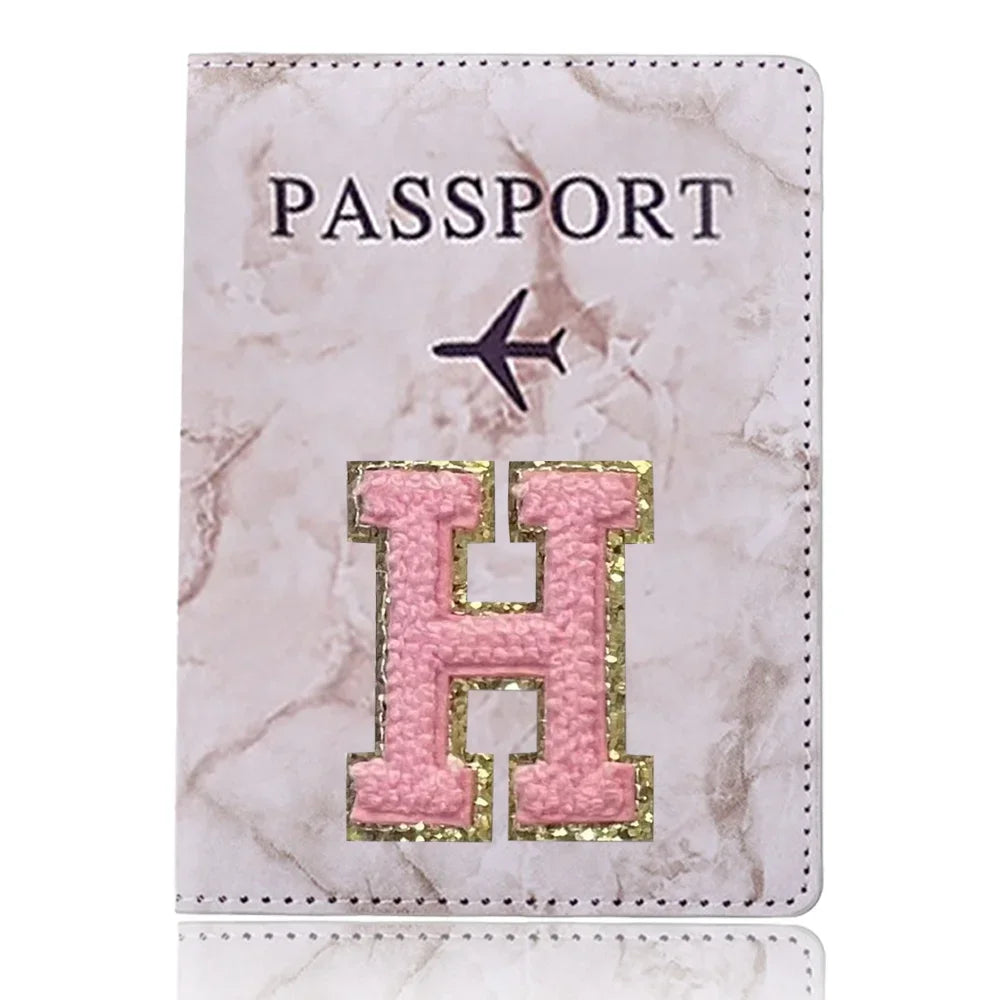 Una funda de pasaporte de imitación de cuero rosa claro con detalles dorados y un diseño de avión negro.