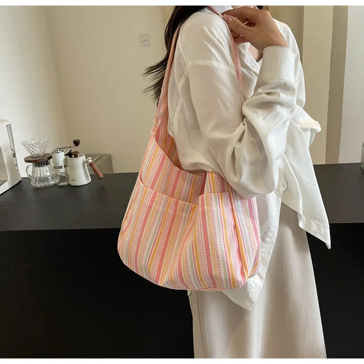 A woman holds a striped canvas shoulder bag with a pink and white pattern against a light background.