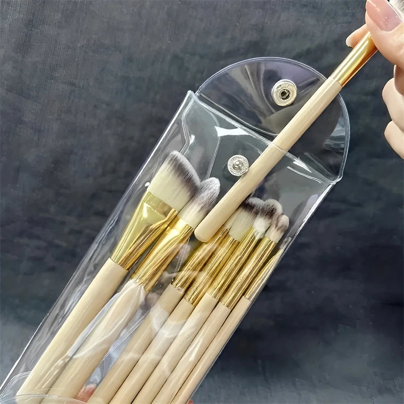 A transparent portable organizer pouch holds several makeup brushes with wooden handles and gold ferrules.