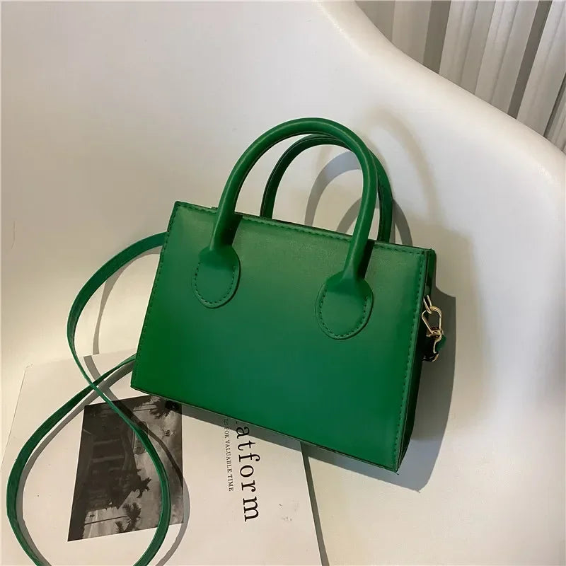Sac à main en cuir PU vert foncé minimaliste avec poignée supérieure, posé sur une surface blanche.