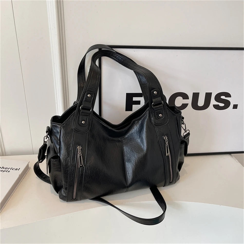 Un sac cabas en cuir noir à multiples poches, présenté sur une surface blanche à côté d'un panneau encadré.