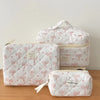 A set of three white quilted cosmetic bags with pink ribbon details resting on a wooden surface.