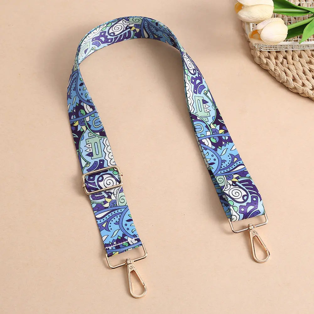 A purple and blue bohemian printed crossbody strap with gold-toned hardware is displayed on a neutral background.