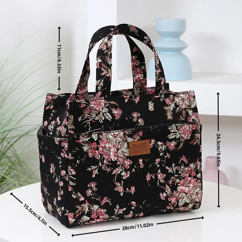 A black cloth tote bag with a pink floral pattern is displayed on a white surface.