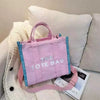 A pink tote bag is displayed next to a cream sweater and a white cushion.