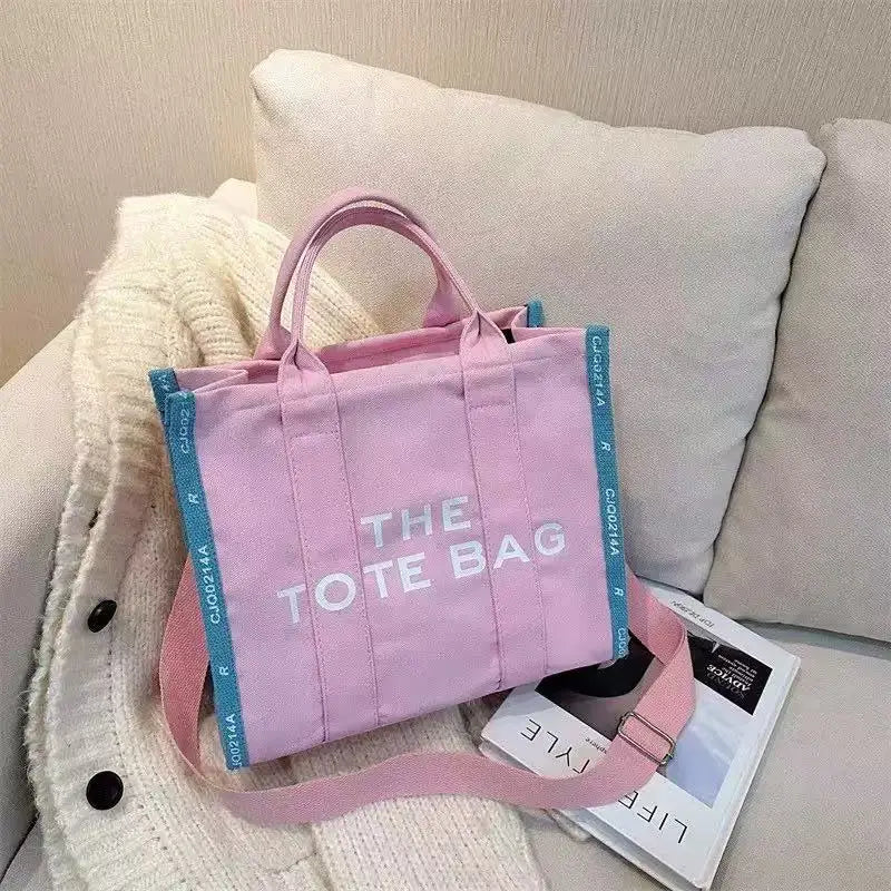 A pink tote bag is displayed next to a cream sweater and a white cushion.