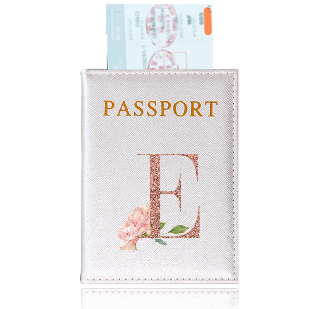 A pink leather passport holder with a gold embossed letter E and a floral design.