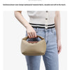 A person is holding a beige nylon dumpling crossbody shoulder bag against a light background.