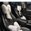 A white plush bowknot headrest pillow and lumbar support placed on a black car seat.