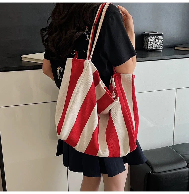 A person is holding a red and white striped canvas tote bag with an inner pocket against a white cabinet.