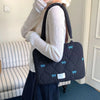 Una persona sostiene un bolso de hombro para portátil acolchado negro con detalles de lazo azul claro.