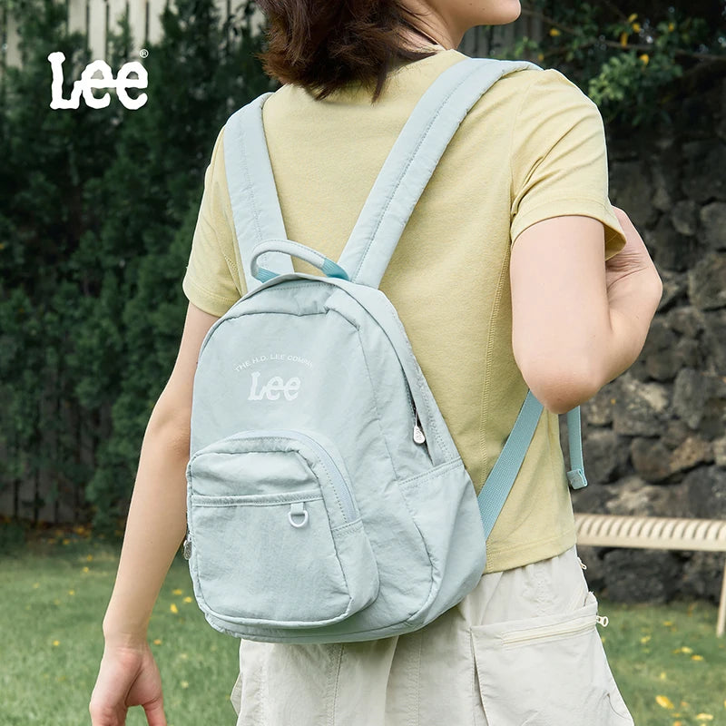 A person wearing a light green backpack is shown outdoors in a natural setting.