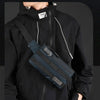 A person wearing a black hoodie holds a dark blue multifunctional chest bag across their chest.