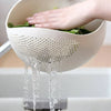 A hand is pouring water from a perforated white plastic basket into a drain.