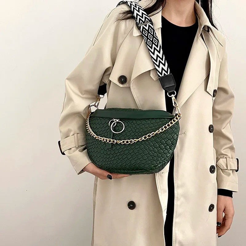 A beige trench coat features a dark green quilted woven pattern waist bag with a black and white patterned strap.