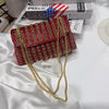A red and gold rhinestone leather evening clutch bag lying on a white surface next to some books.