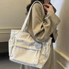 Une personne tient un sac en toile de daim beige à multiples poches, montrant la texture et la structure du tissu.
