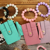 A collection of silicone and PU leather key chain wristlet wallets in pastel colors, displayed on a wooden surface.