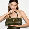 A woman holds a dark olive green vegan leather tote bag with gold hardware against a white background.