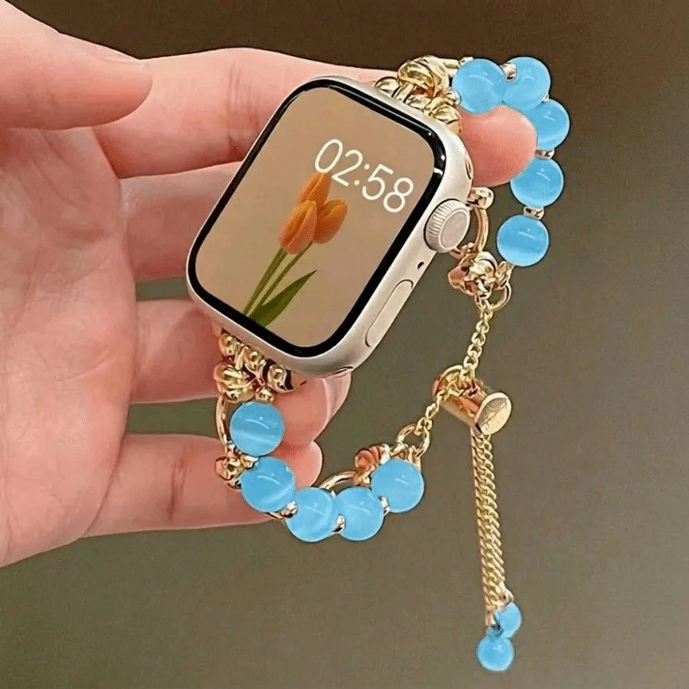 Eine Hand hält eine Apple Watch mit 02:58, verbunden mit einem verstellbaren Metallarmband mit hellblauen Kristallperlen.