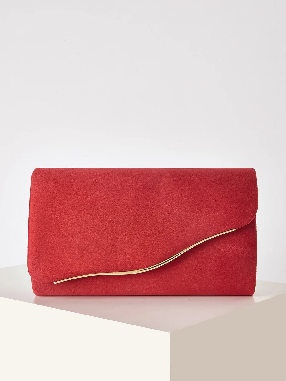 A vibrant red velvet evening clutch with a gold-toned detachable shoulder strap resting on a white surface.