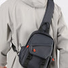 Un homme portant une veste grise transporte un sac de sport bleu marine sur son dos.