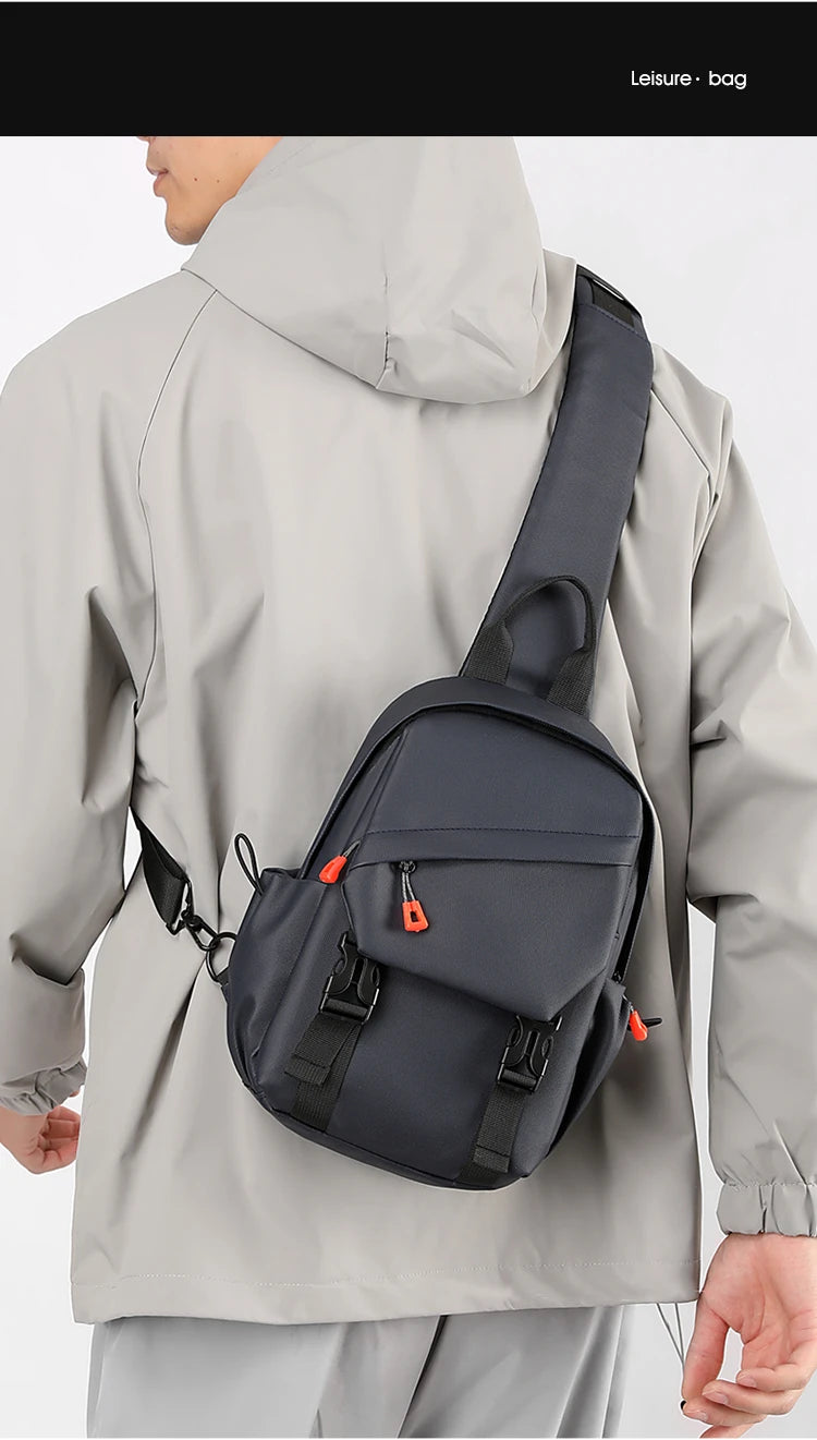 Un homme portant une veste grise transporte un sac de sport bleu marine sur son dos.
