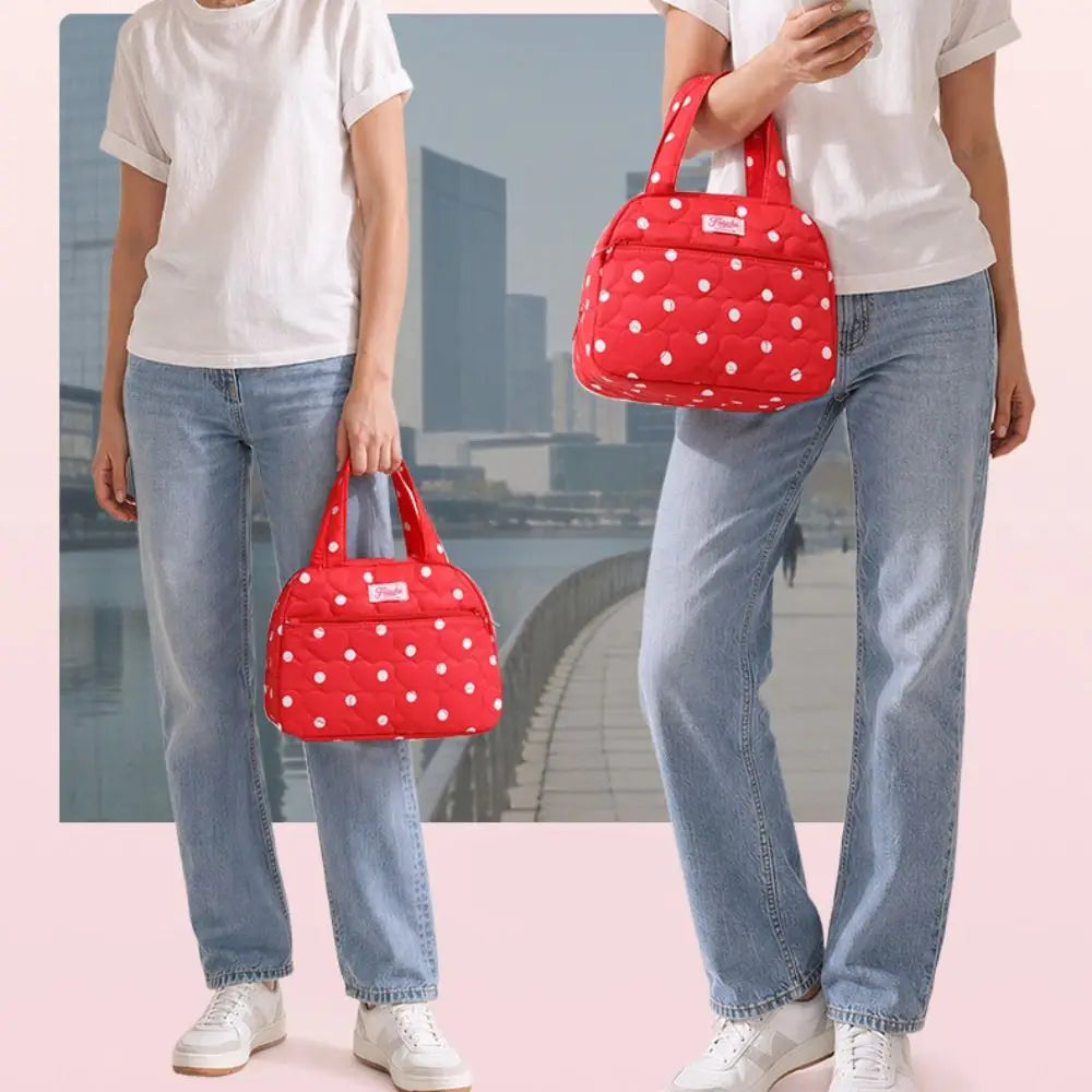 A woman is holding a red polka dot insulated lunch tote bag against a light pink background.