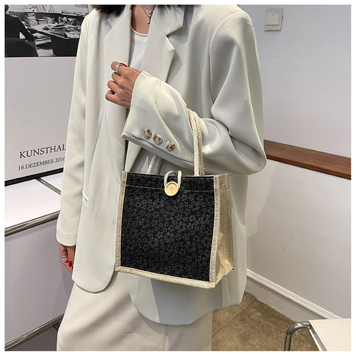 A woman holds a light beige blazer and a black and cream floral linen tote bag.