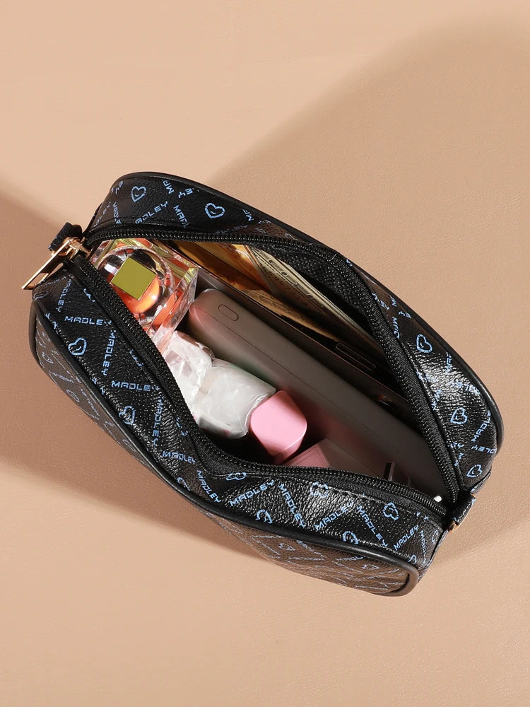 A black leather fashion crossbody bag is open, showing a smartphone and perfume bottle inside.
